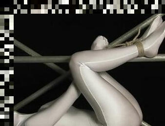 Encased girl in shiny zentai suit is tied to a metal pole and tries to escape