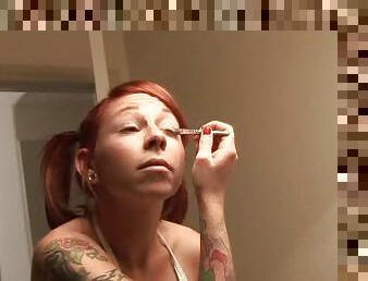 Heavily tattooed redhead with pigtails puts on makeup