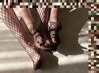 The girl caresses her legs in fishnet tights and strokes them with her hands in lace gloves