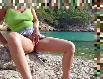 girl peeing on a public beach on a rock near the water